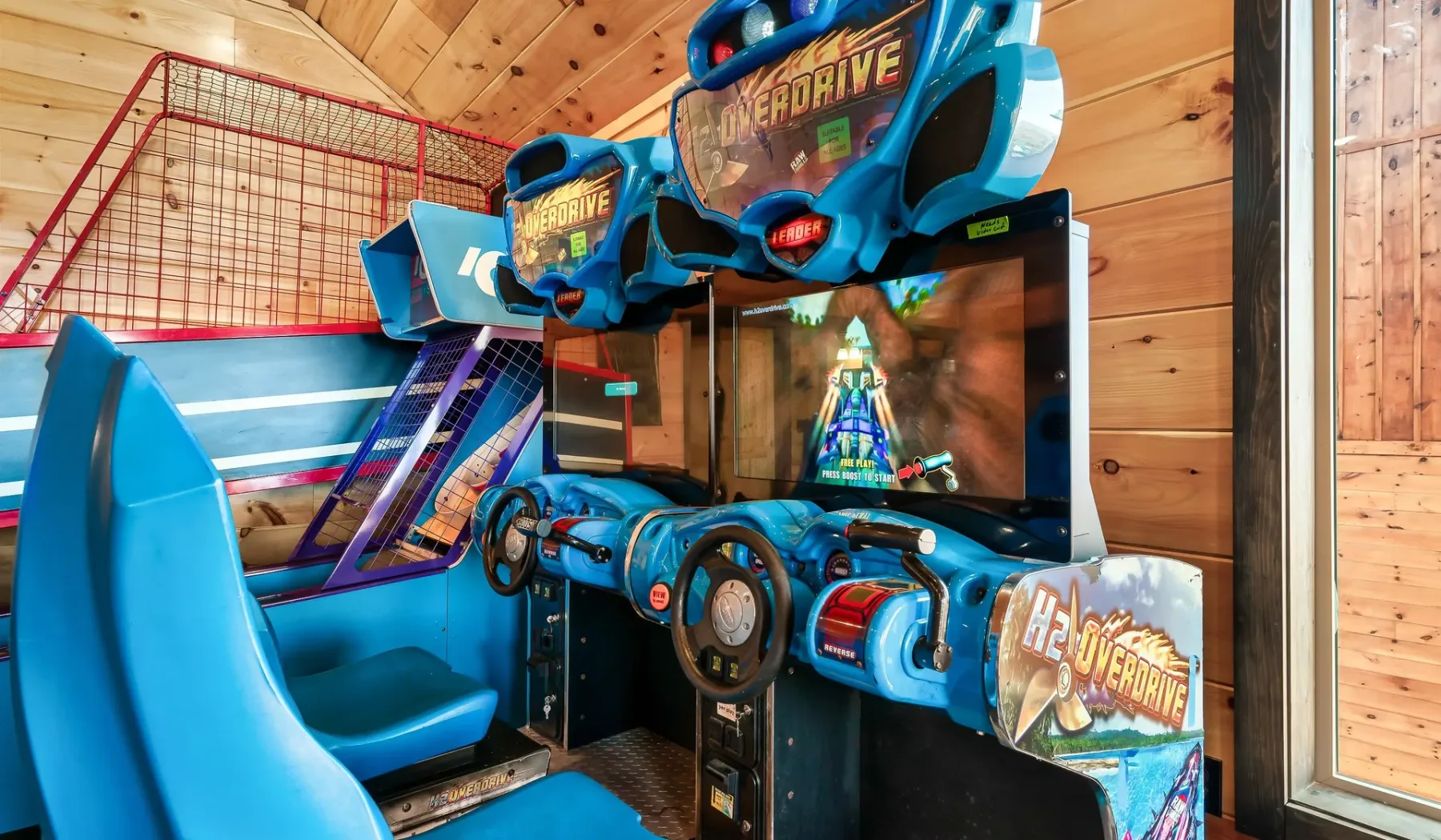 Una máquina arcade de carreras está junto a una cabina de juego azul en una sala revestida de madera.