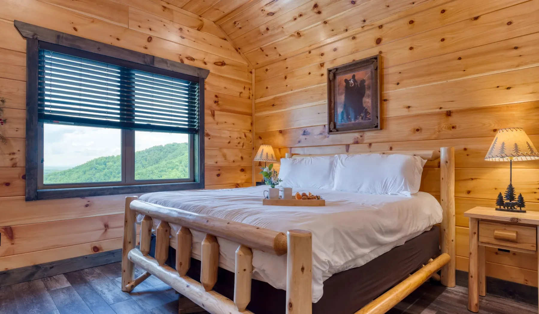 Un dormitorio con cama de madera, ropa de cama blanca y una ventana con vistas a colinas verdes.