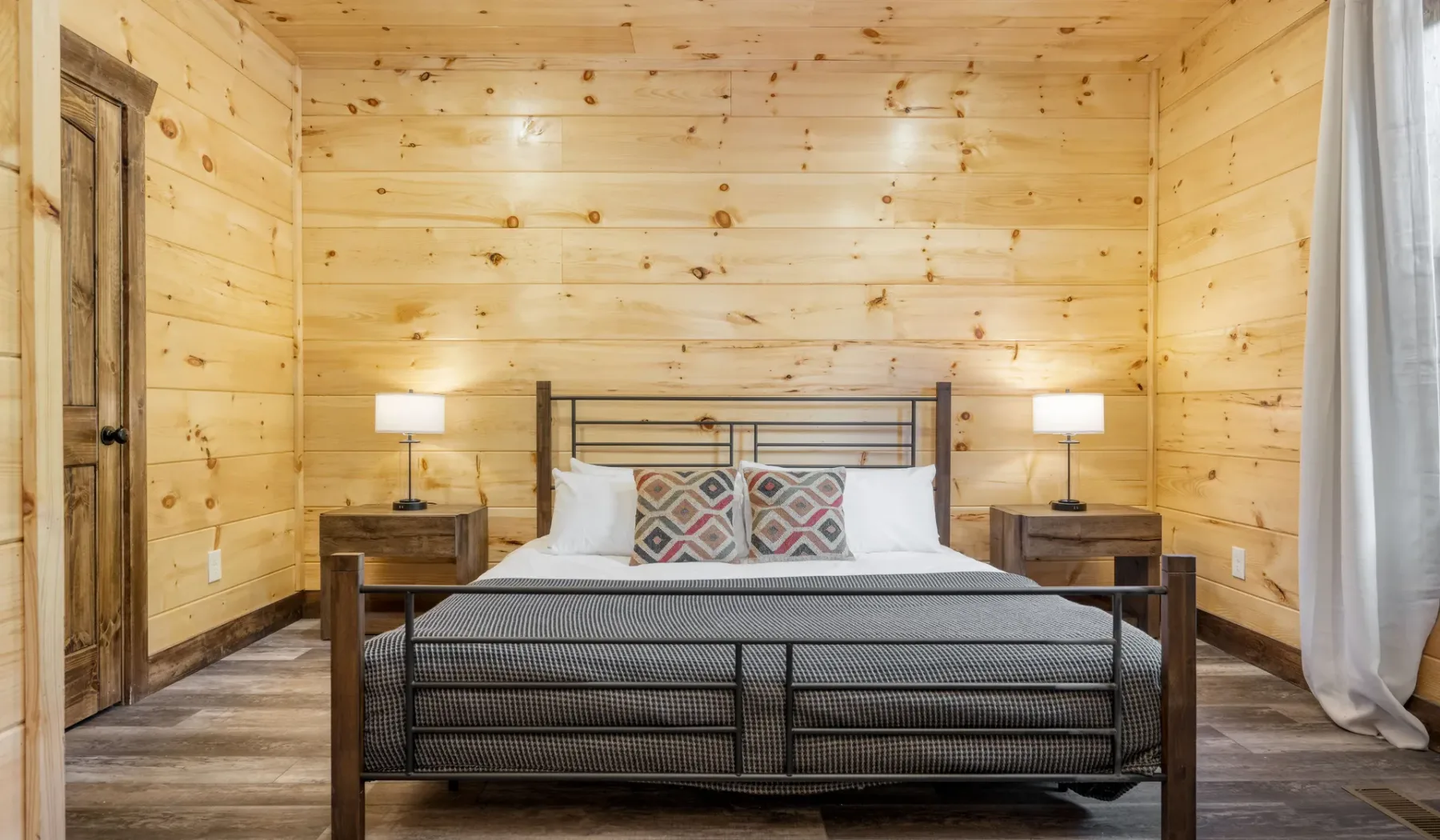 Un dormitorio con una cama, almohadas estampadas y paredes revestidas de madera clara.