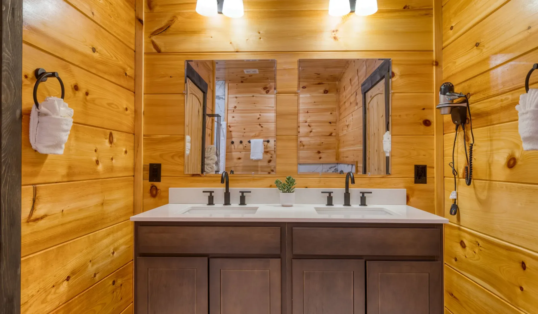 Un baño revestido de madera con un tocador de doble lavabo y un espejo amplio.