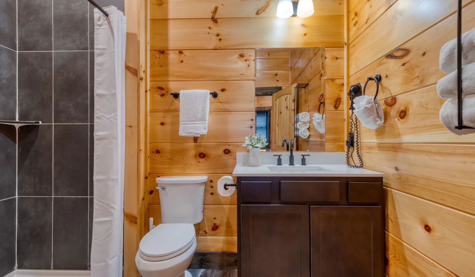 Un baño revestido de madera con lavabo, tocador e inodoro.