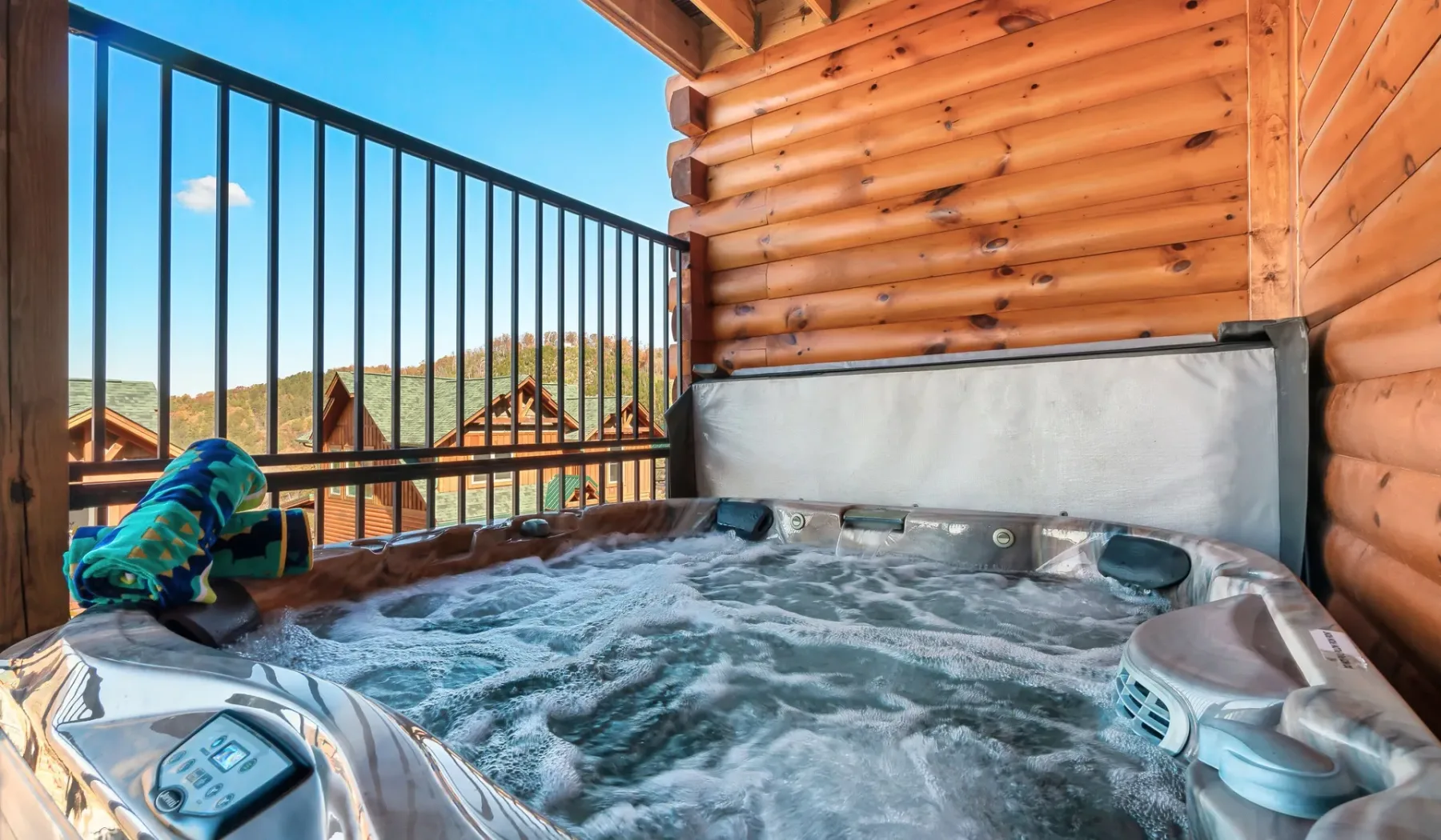 Una bañera de hidromasaje al aire libre está junto a una pared de cabaña de madera y una barandilla.
