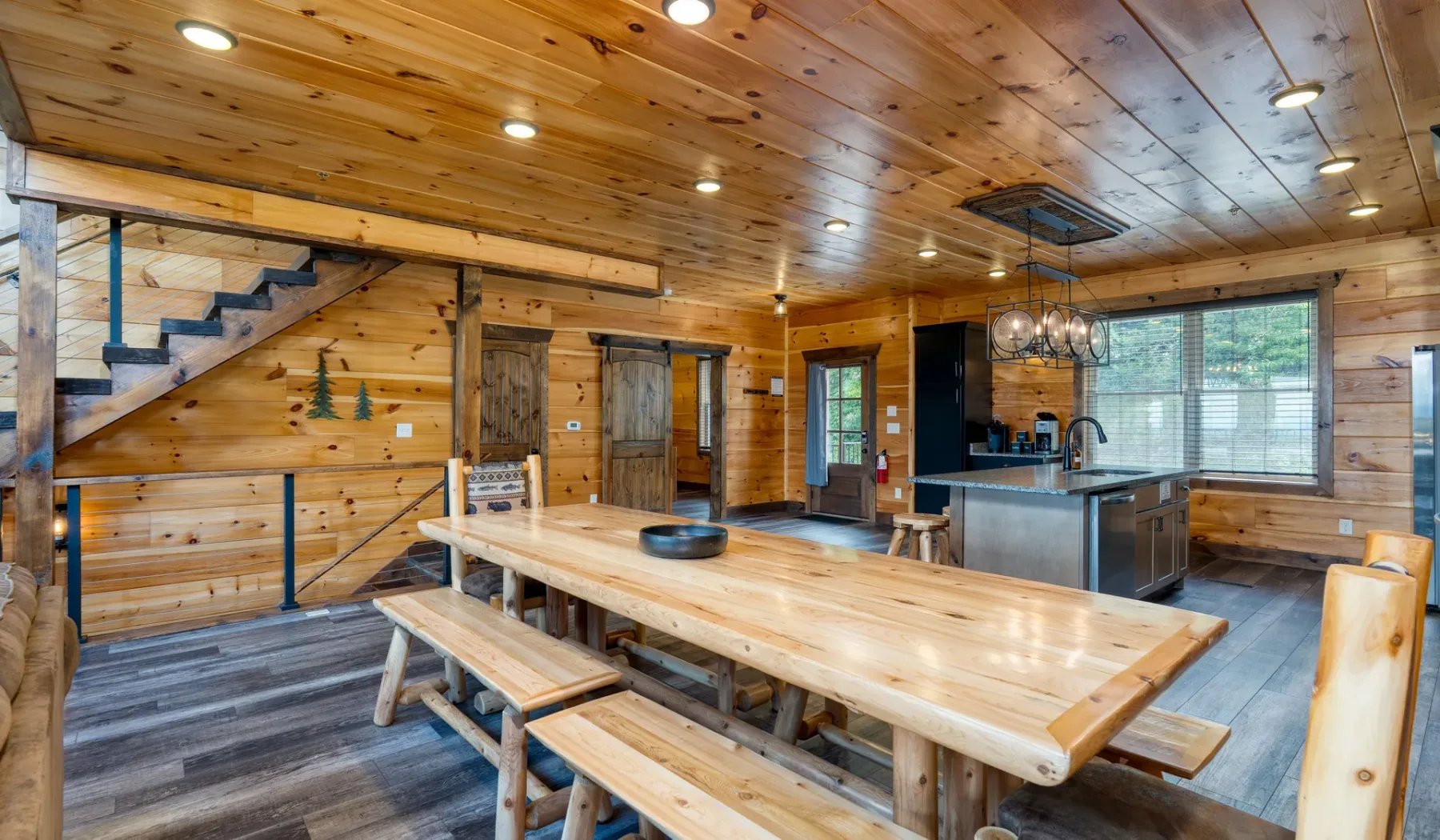 Zona de comedor y cocina revestida de madera, con una mesa larga e isla.