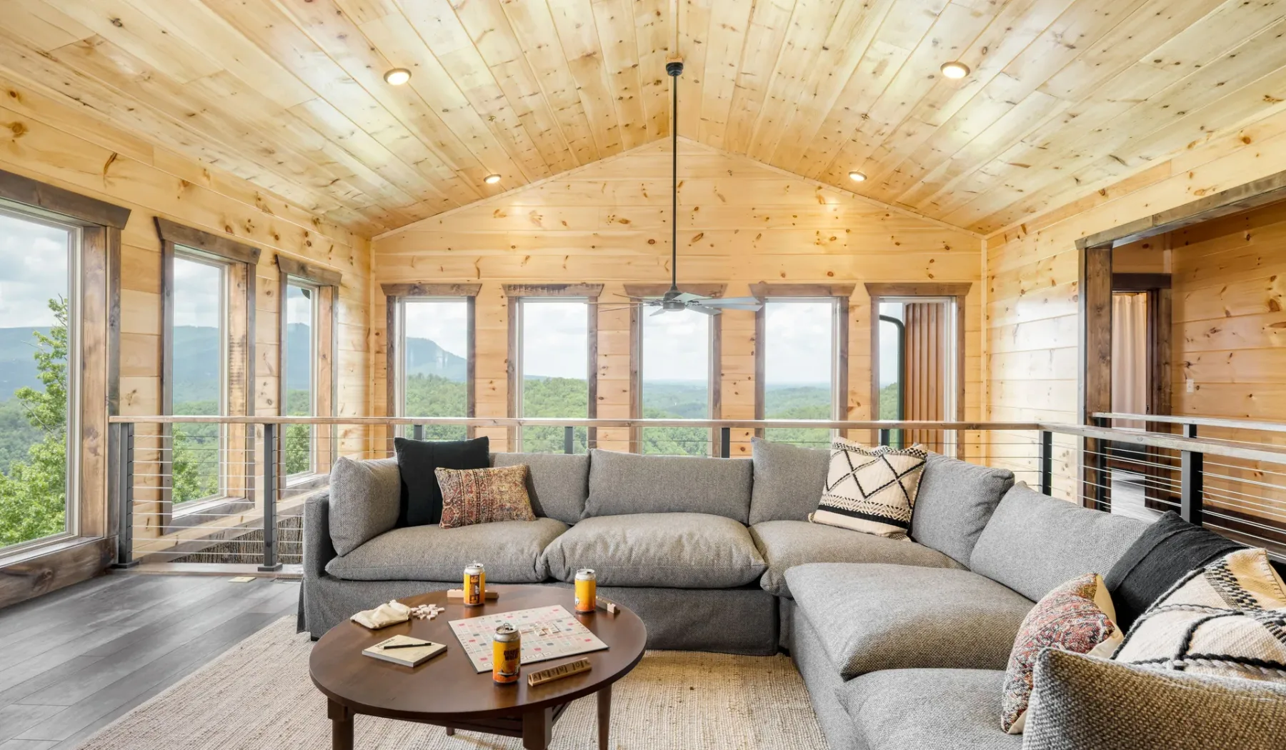 Una sala de estar revestida de madera, con asientos seccionales y grandes ventanas con vistas a la vegetación.