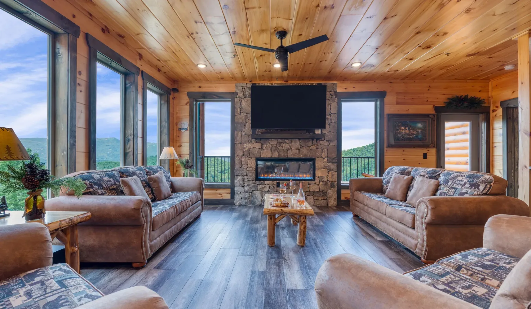 Una sala con paredes de madera tiene sofás frente a una chimenea de piedra y un televisor.