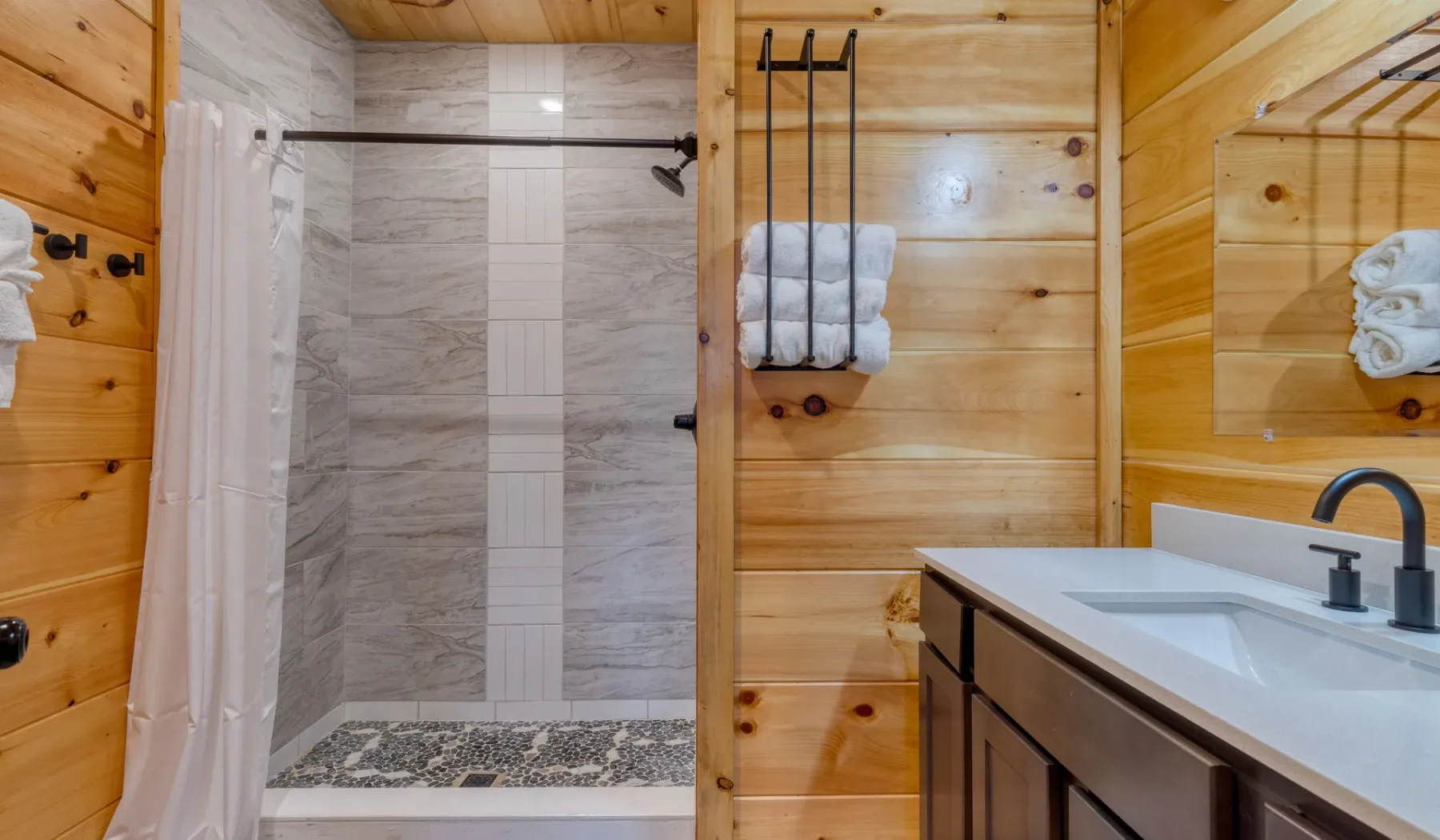 Un baño con ducha alicatada, paredes revestidas de madera y un lavabo con mueble.
