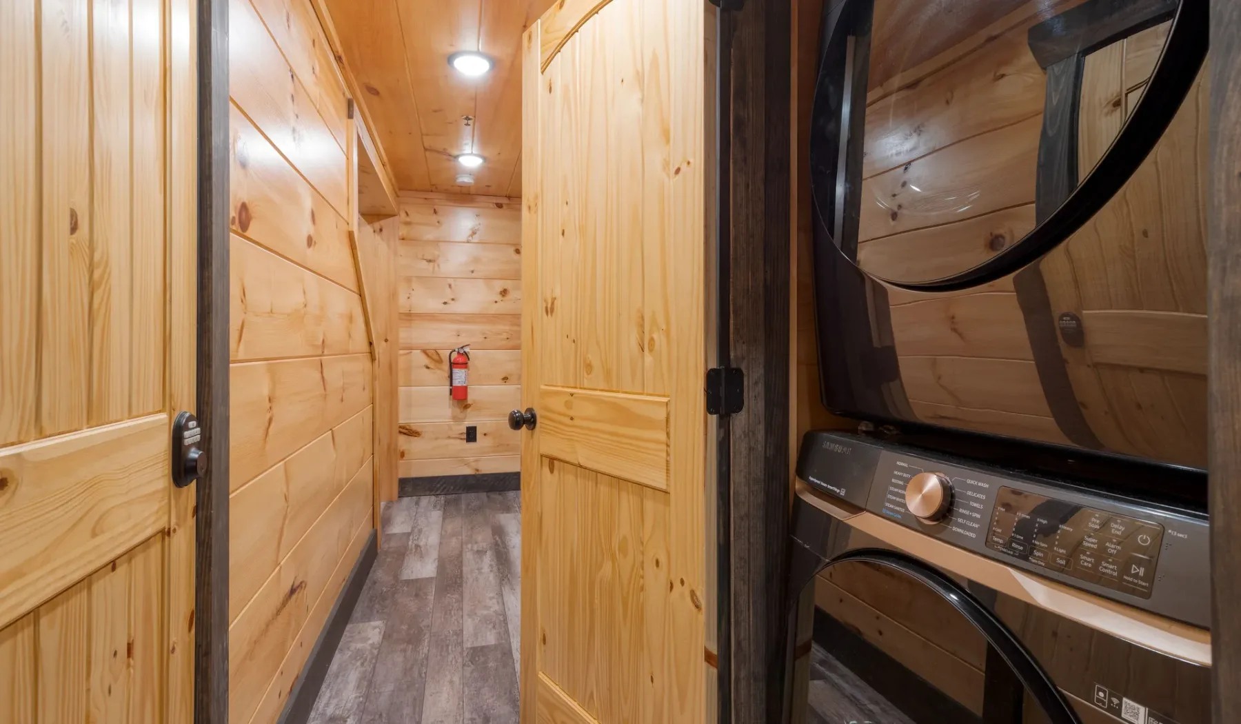 Pasillo revestido de madera con una lavadora y secadora apiladas junto a la puerta.