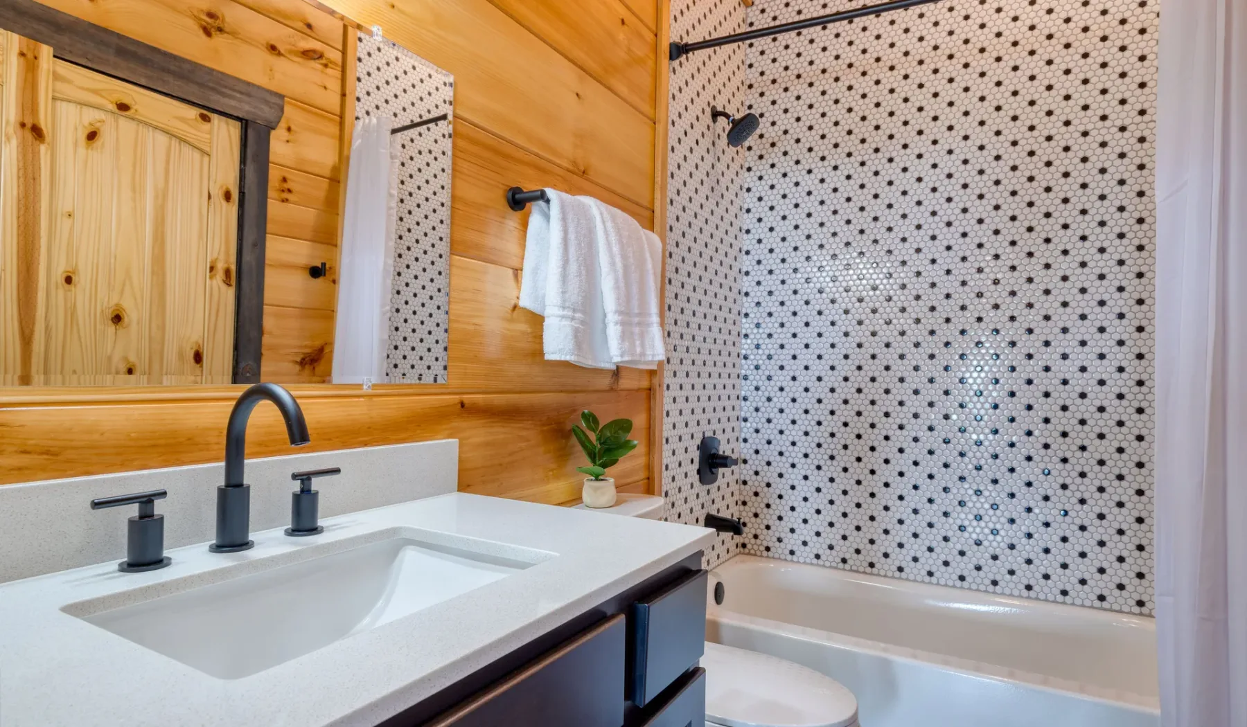 Un baño revestido de madera con lavabo, espejo y pared de ducha estampada.