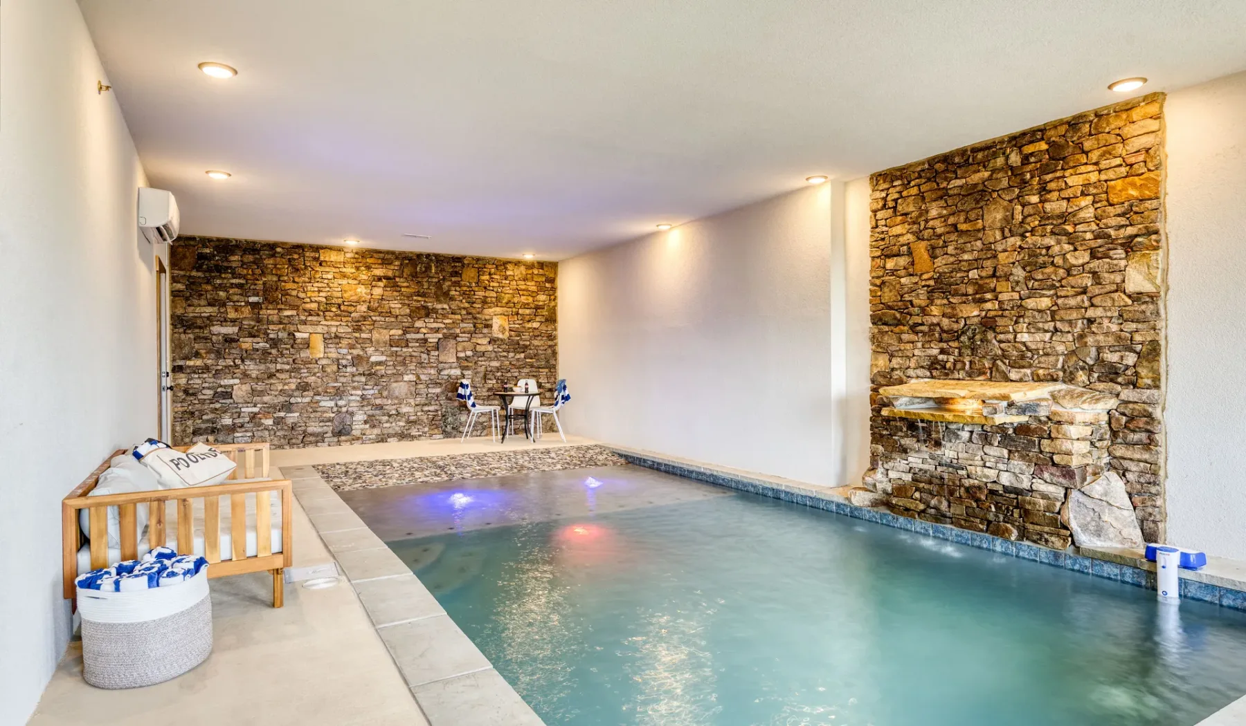 Una piscina interior está junto a paredes de piedra y un banco de madera.