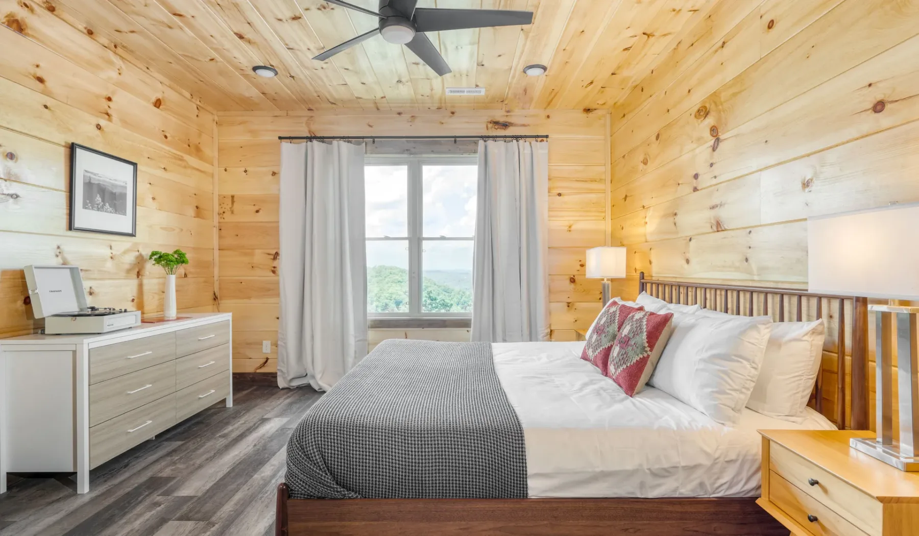 Un dormitorio con una cama, paredes revestidas de madera clara y una ventana con vistas al agua.
