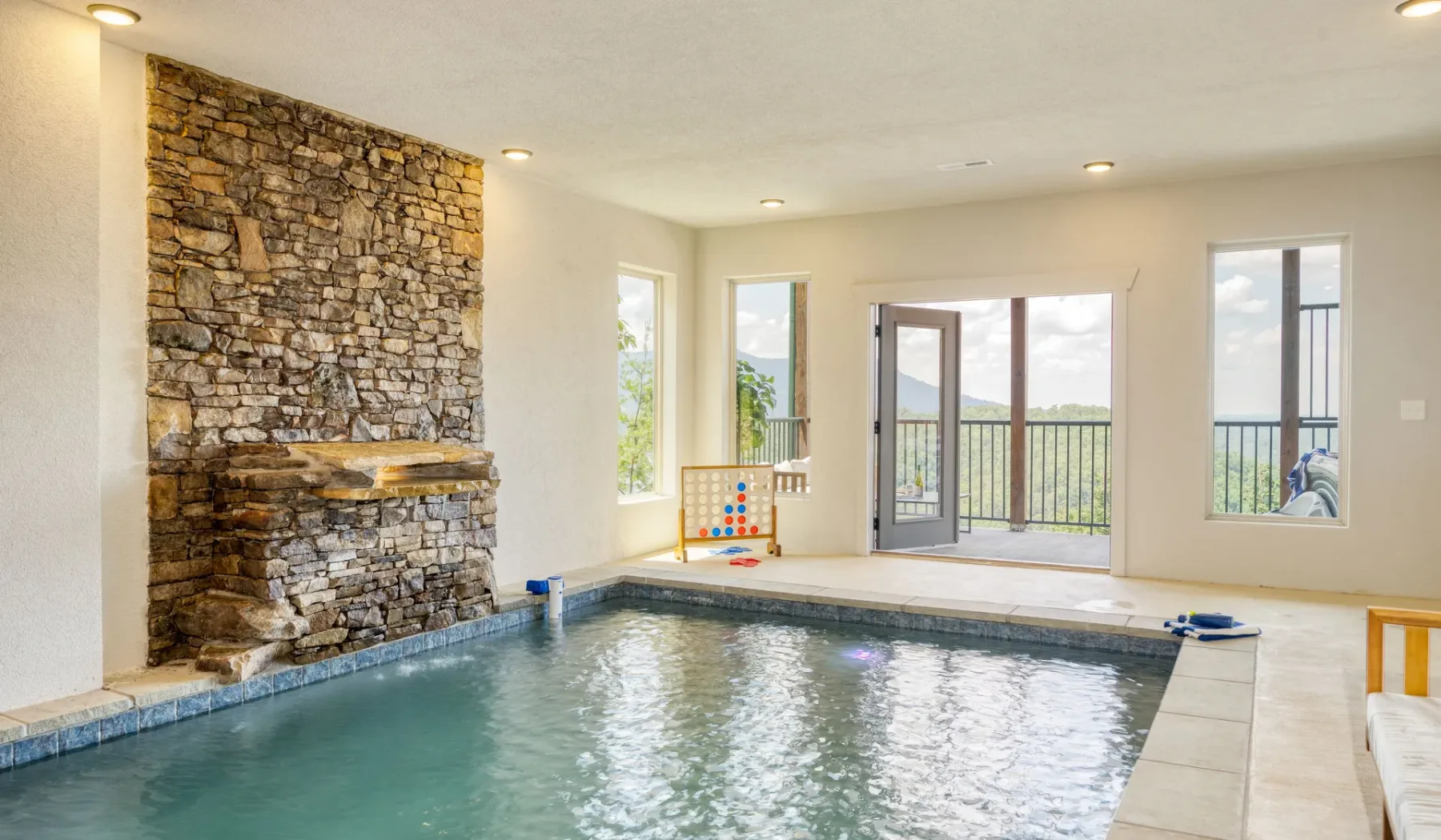 Piscina interior junto a una pared de piedra, con puertas que dan a un balcón.