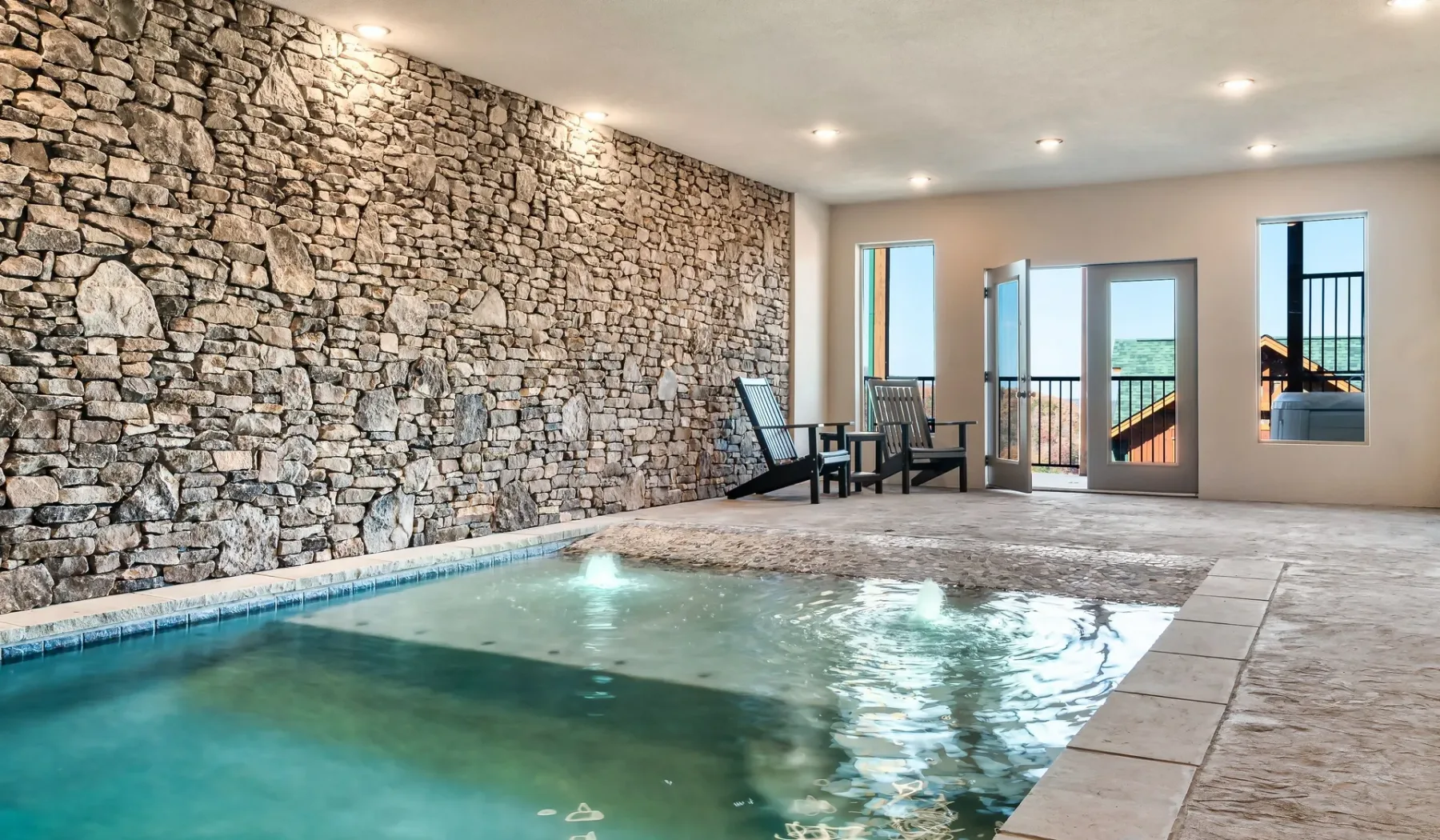 Piscina interior junto a una pared de piedra, con asientos cerca de las ventanas.