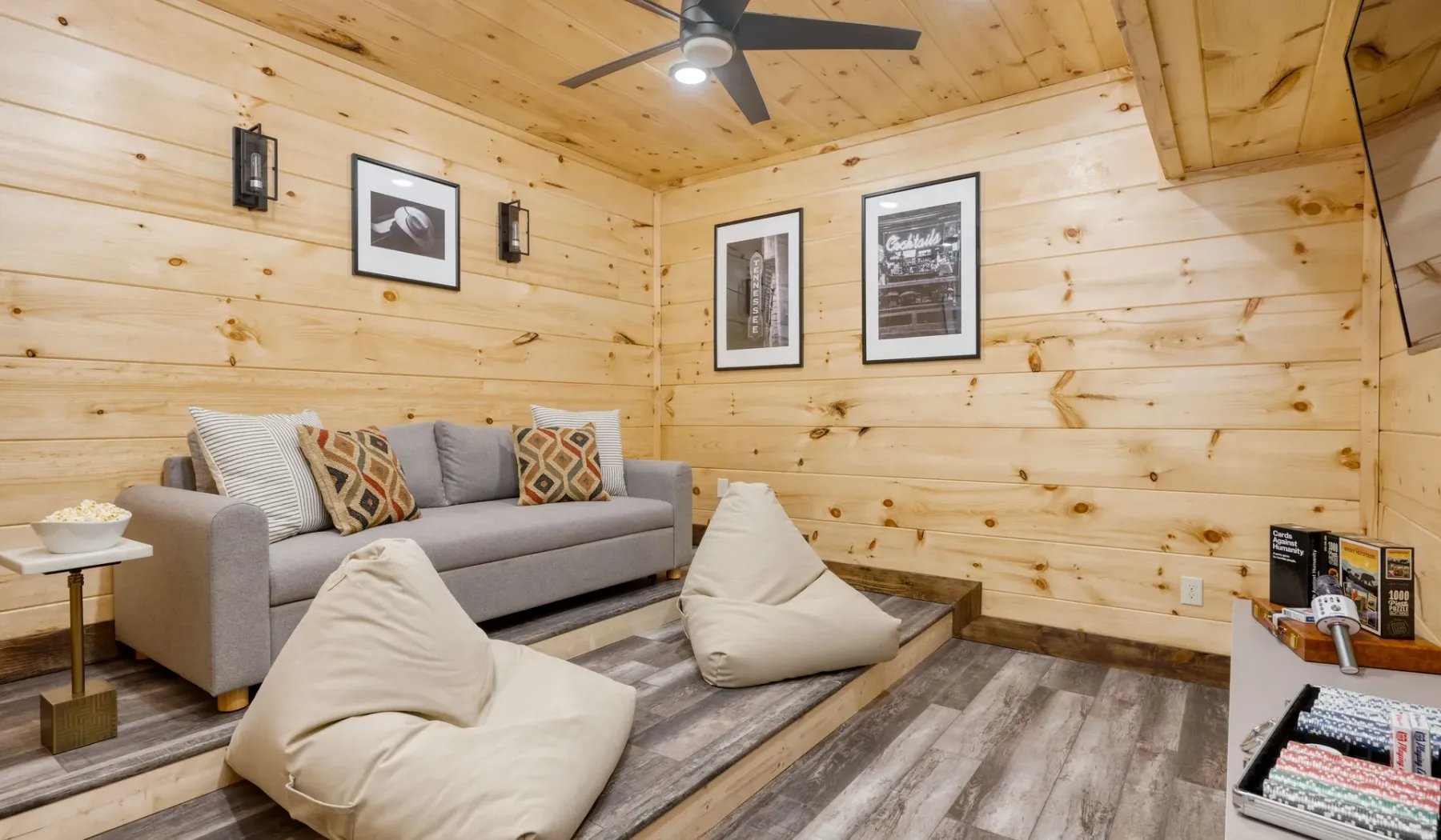 Sala de estar revestida de madera con un sofá gris y cojines de suelo.