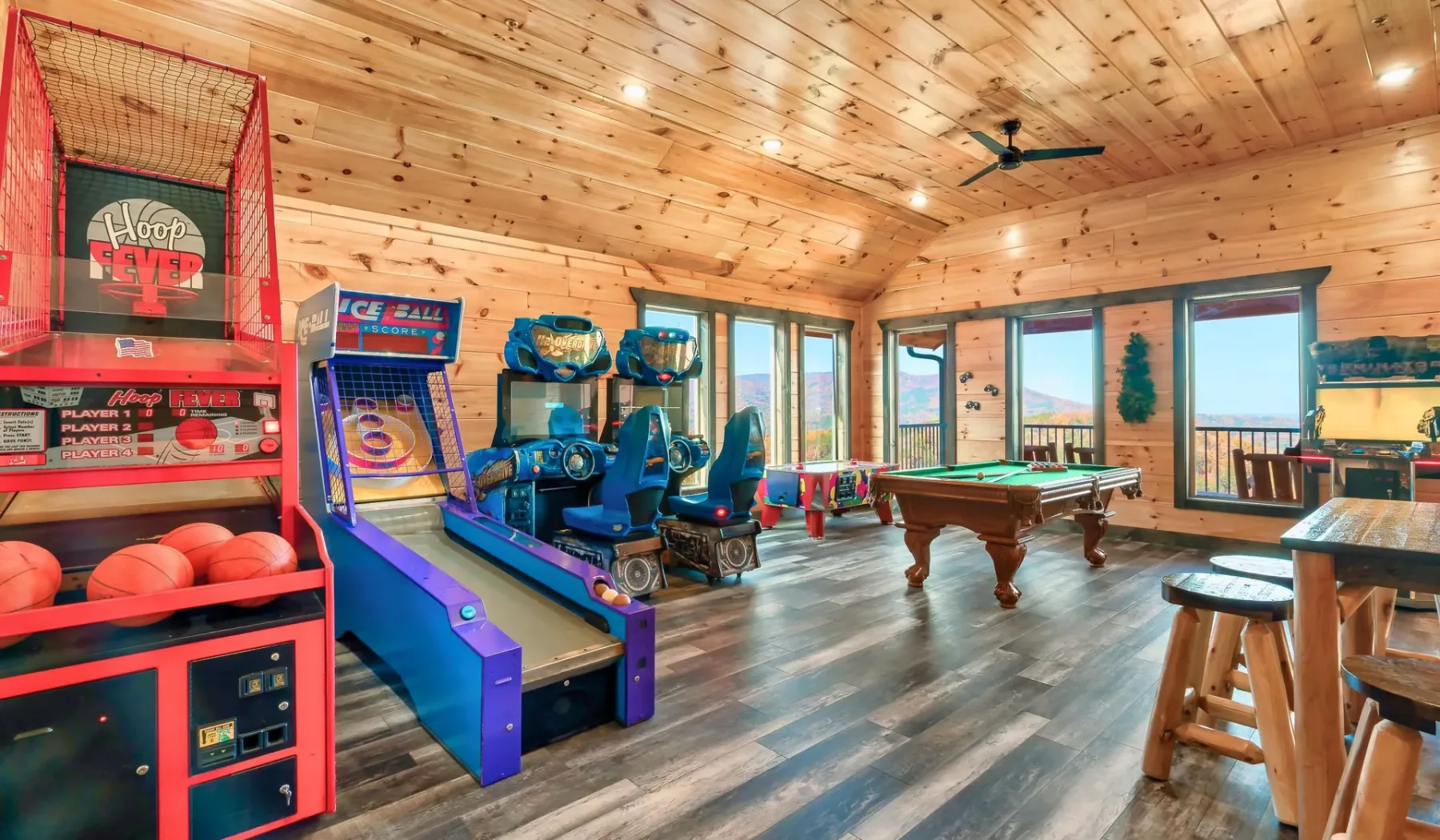 Una sala de juegos revestida de madera, con máquinas recreativas, una mesa de billar y ventanales.