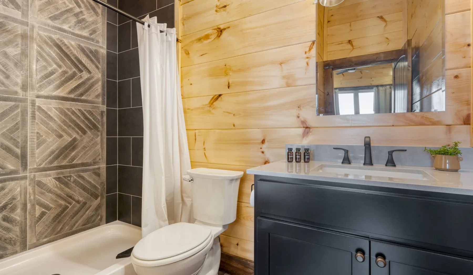 Un baño con pared revestida de madera, bañera, inodoro y tocador oscuro.
