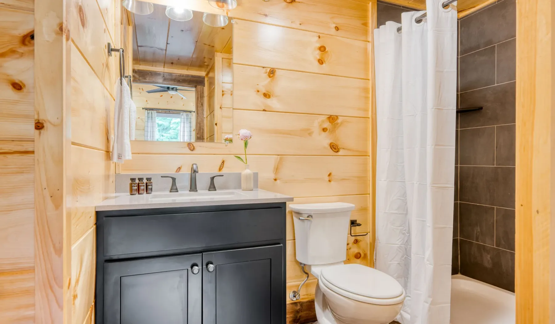 Un baño con un mueble oscuro, espejo, inodoro y cortina de ducha.