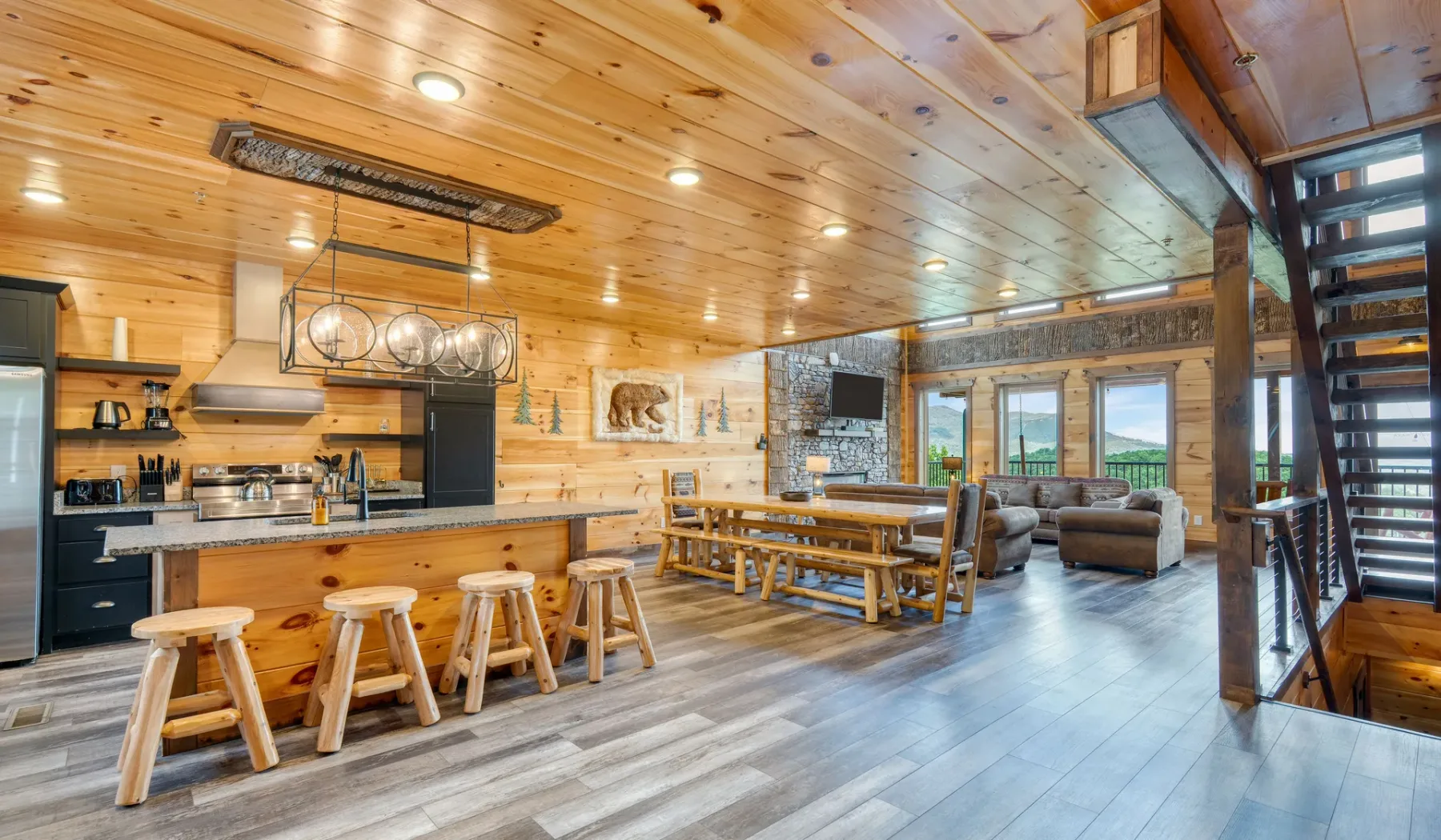 Una cocina y sala de estar de planta abierta, revestidas de madera, con una mesa larga.