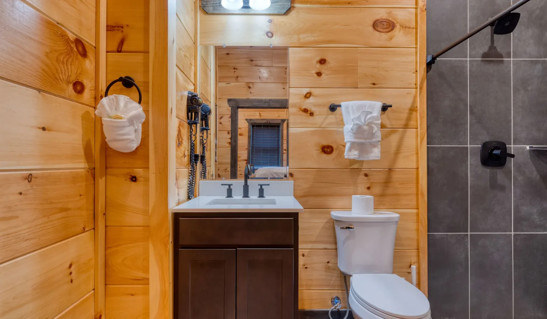 Baño revestido de madera con lavabo, espejo e inodoro.