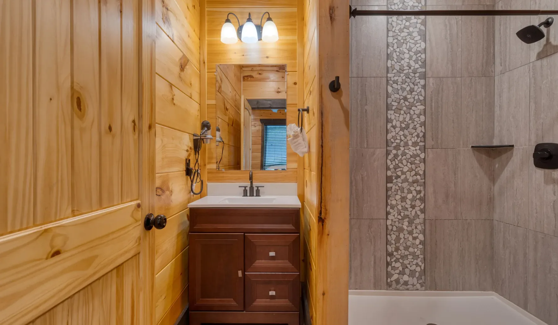 Un baño revestido de madera con un tocador junto a una ducha alicatada y una bañera.
