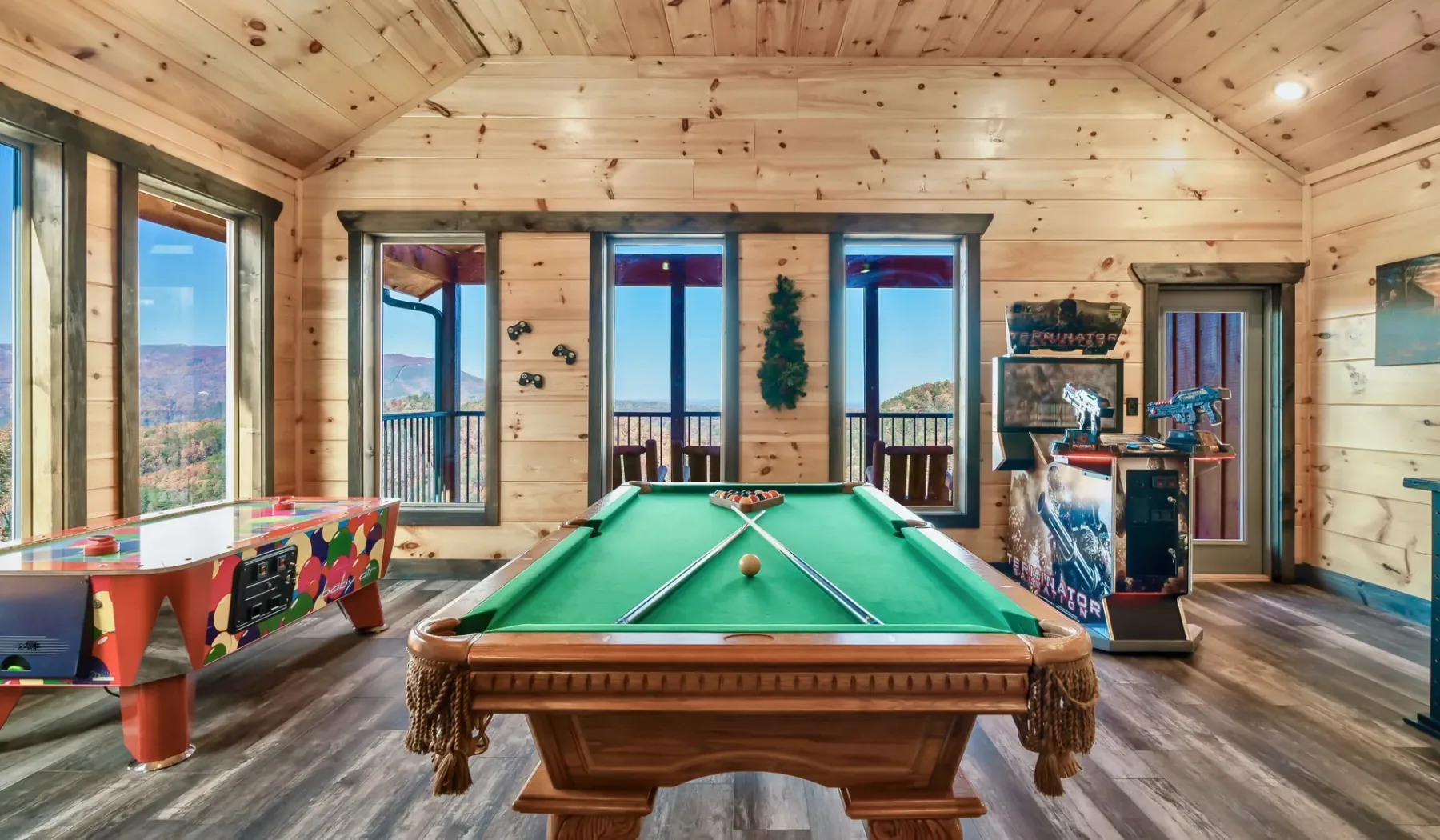 Una sala de juegos con mesa de billar, máquinas recreativas y grandes ventanas.