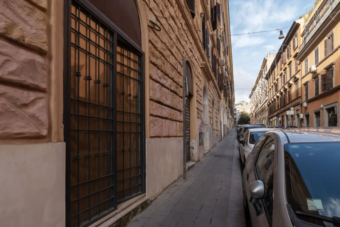 Una calle urbana estrecha bordeada de coches estacionados y edificios altos.