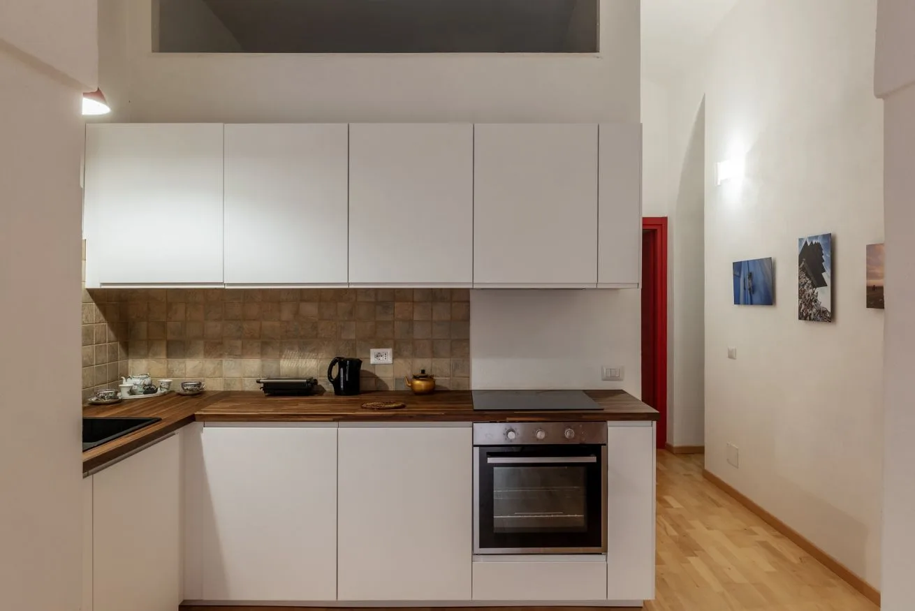 Una cocina compacta con gabinetes blancos, un salpicadero de azulejos y un horno.