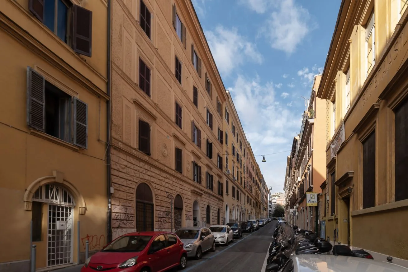 Una calle estrecha de ciudad flanqueada por edificios altos y coches aparcados.
