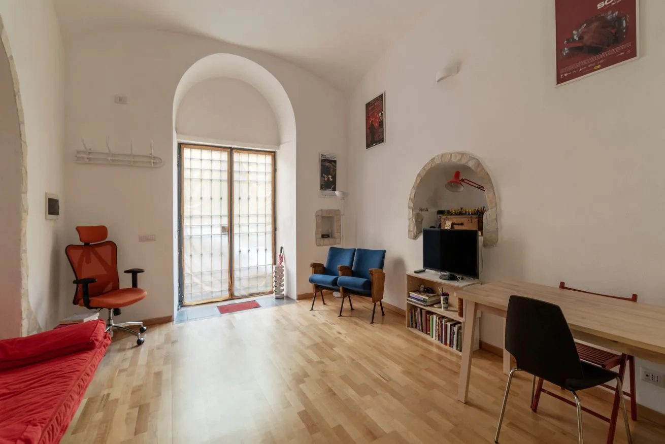 Una habitación luminosa con una puerta de vidrio arqueada, asientos y un televisor.