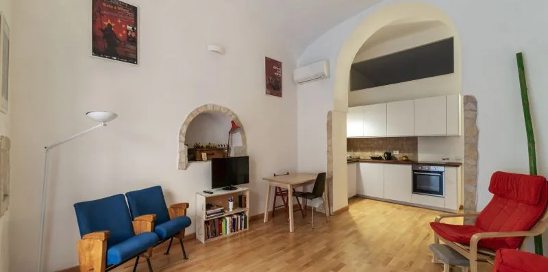 A living area with blue seating, a television, and an adjoining kitchen.