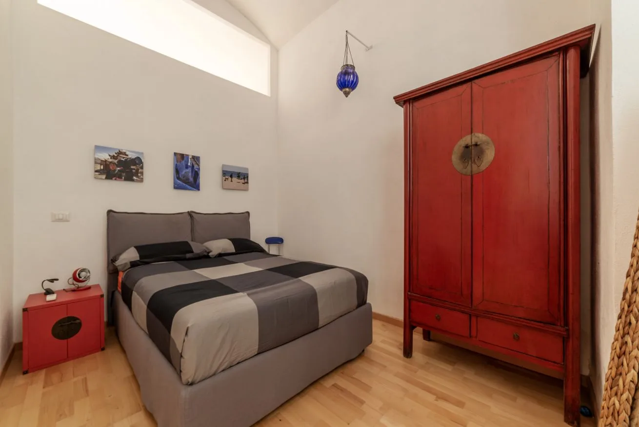 Un dormitorio con una cama doble, ropa de cama estampada y un armario rojo.