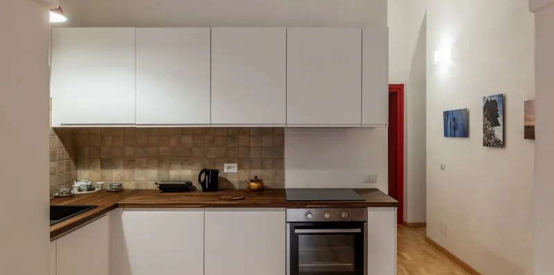 Una cocina compacta con gabinetes blancos, un salpicadero de azulejos y un horno empotrado.