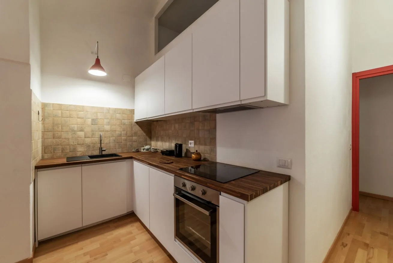 Una cocina compacta con gabinetes blancos, encimeras de madera y un horno integrado.