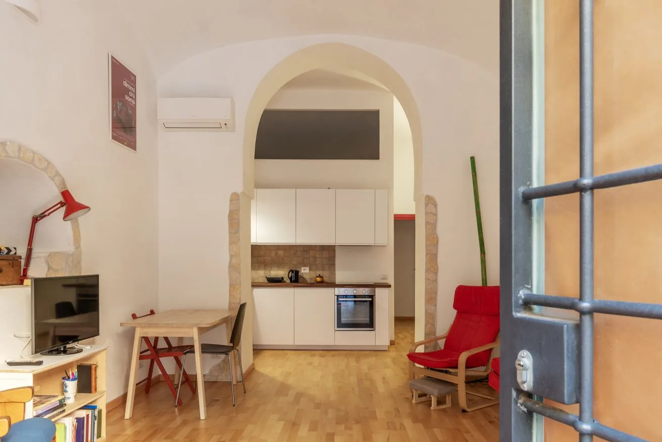 Una habitación luminosa con una pequeña cocina al fondo y un televisor.