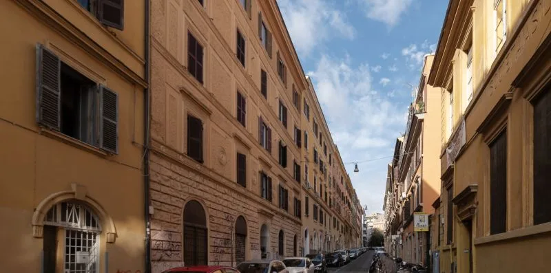 Una calle estrecha de la ciudad flanqueada por edificios altos bajo un cielo parcialmente nublado.