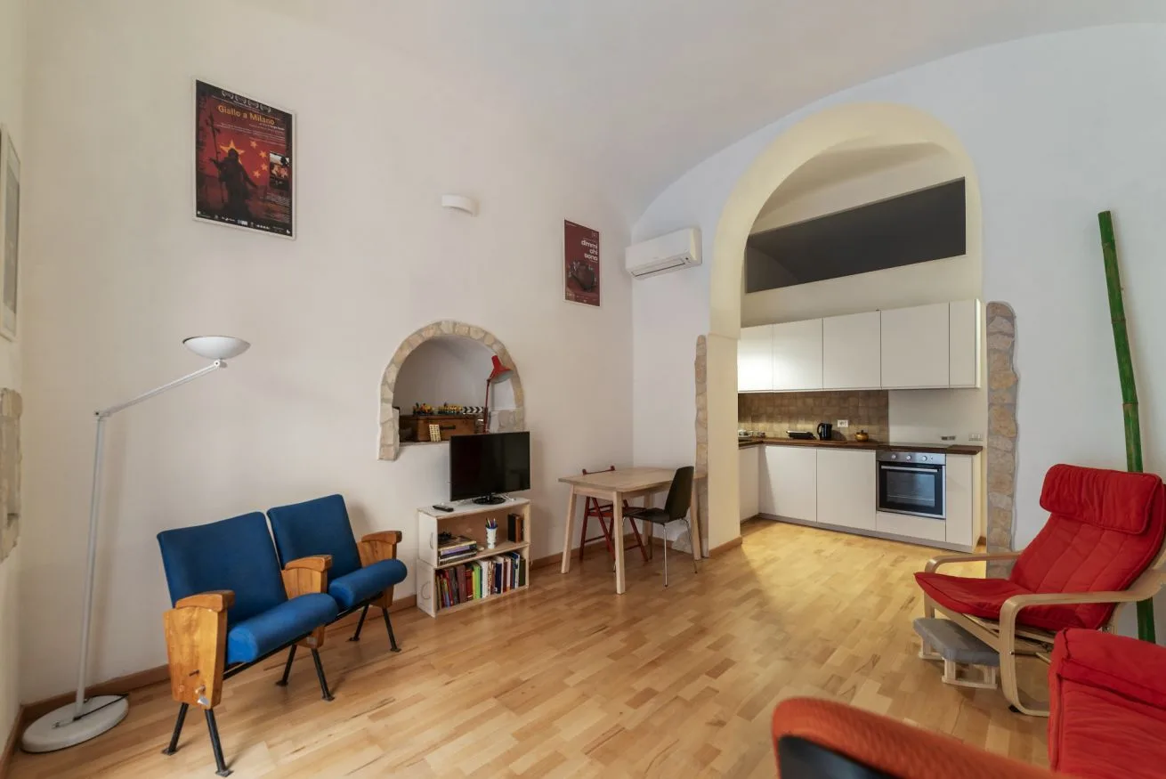 Una sala de estar con asientos azules y una cocina abierta al otro lado de un arco.