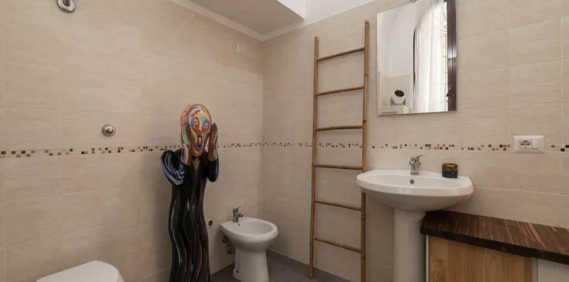 Un baño alicatado con lavabo, espejo y una escultura decorativa.