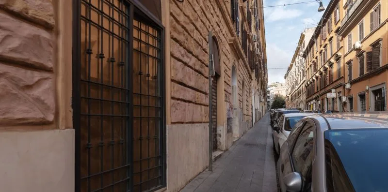 Una calle urbana estrecha flanqueada por coches estacionados y edificios de varias plantas.