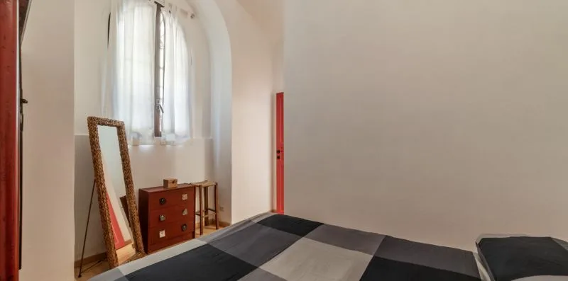 Un dormitorio con una cama junto a una ventana alta y arqueada.