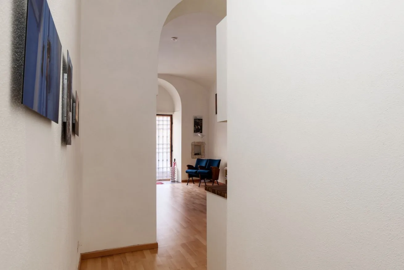 Un pasillo se abre a una habitación luminosa con asientos y una ventana alta.