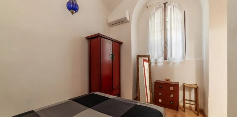 Un dormitorio con cama, armario de madera y ventana arqueada.
