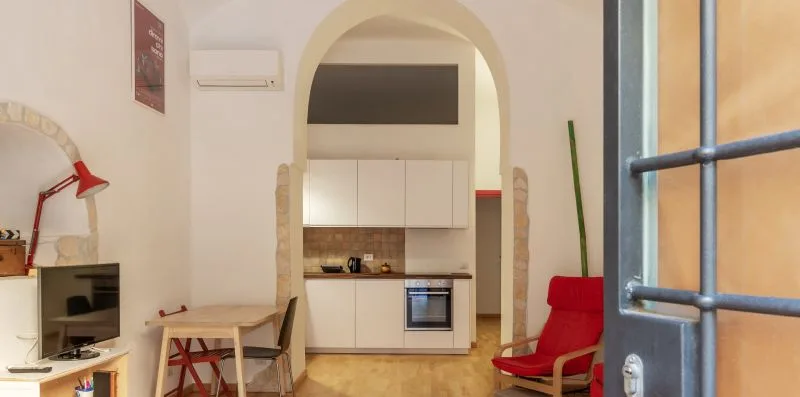 A compact kitchen sits beneath an arched opening, beside a small dining table.