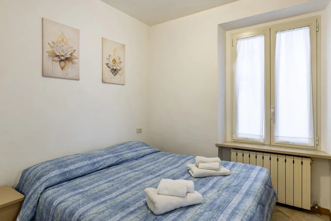 A bedroom with a blue striped bed and a window with light curtains.