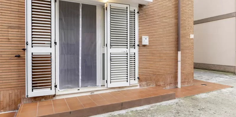 A building entrance with open louvered shutters and a tiled step.
