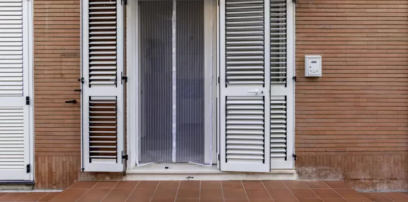 A tiled outdoor terrace in front of a doorway with open shutters.