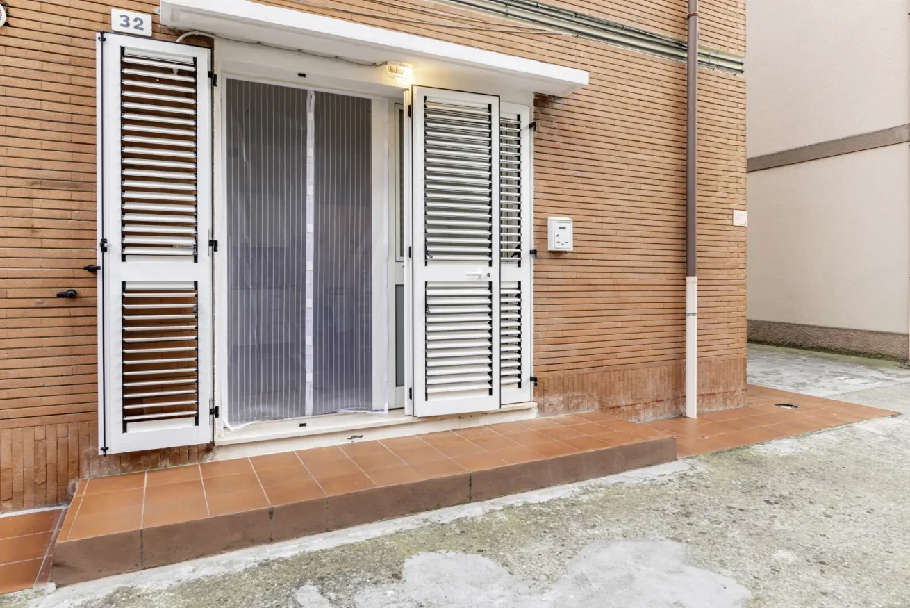 A building entrance with open louvered shutters and a screened doorway.