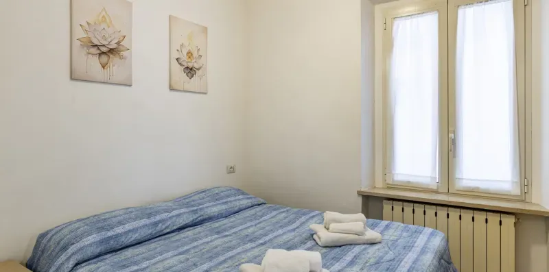 A bedroom with a bed covered in blue-striped bedding beside a bright window.