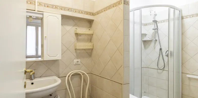 A tiled bathroom with a sink, wall shelves, and a glass shower.