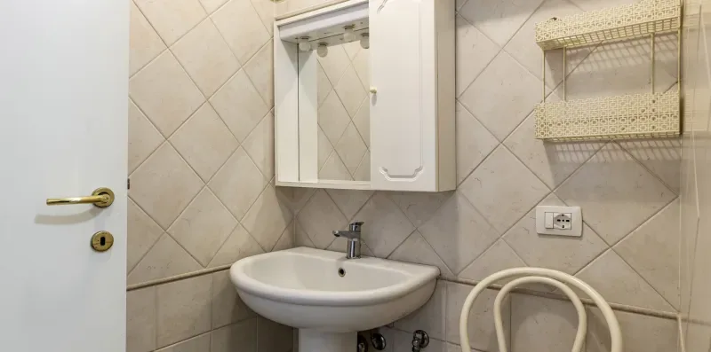 A tiled bathroom with a sink, mirrored cabinet, and wall shelves.