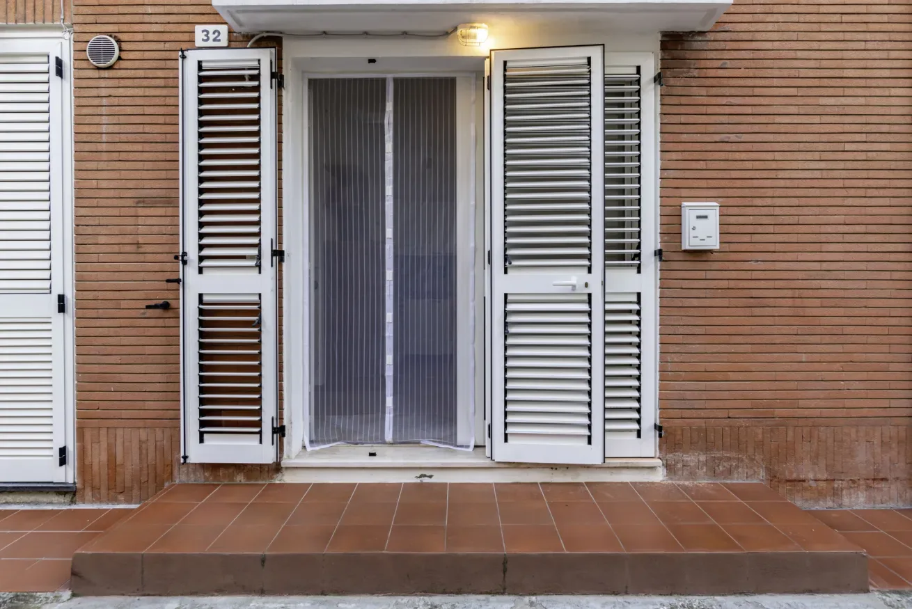 An exterior doorway with open louvered shutters faces a tiled entry landing.