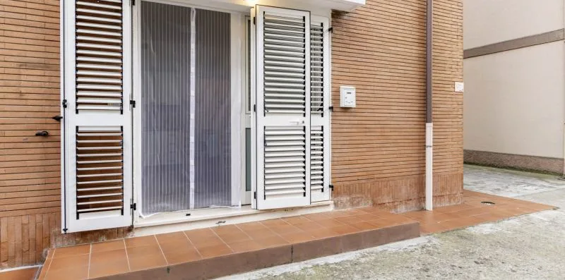 A building entrance has open white louvered shutters beside a screened doorway.